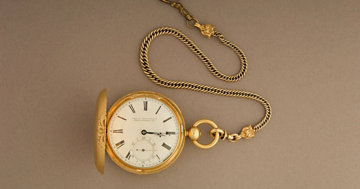 Montre de poche ancienne en or avec sa chaîne, posée sur un fond brun clair